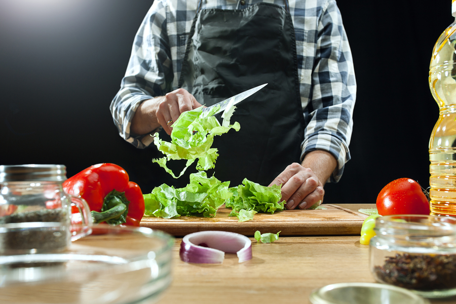 Foto de un hombre cortando hojas de lechuga para preparar una ensalada
